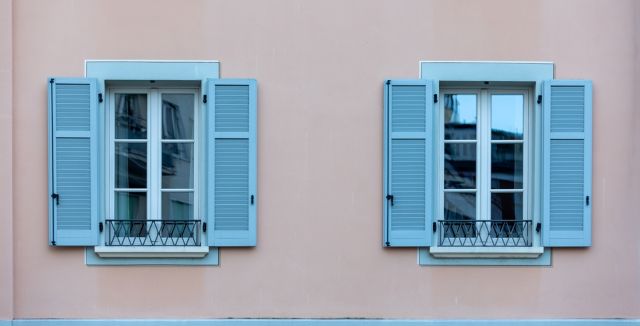 Deux fenêtres aux volets bleus sur un bâtiment rose en France