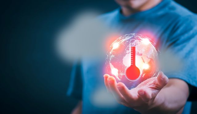 Man in blue T-shirt holds in his hand a globe on fire with a red temperature gage