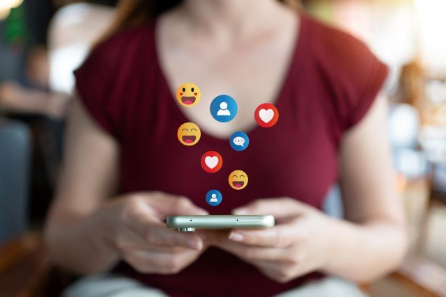 Girl using smart phone with social media emojis emerging from screen