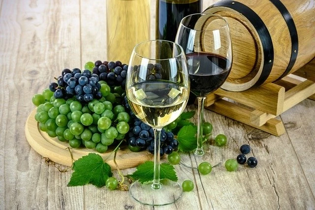  A half full wine glass next to a small keg and some grapes