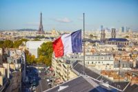 Drapeau français flottant au-dessus des toits parisiens, avec la tour Eiffel au loin, en haut à gauche.