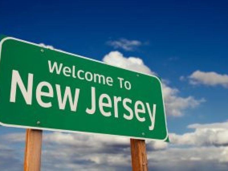 'Welcome to New Jersey' green sign against a blue sky with clouds