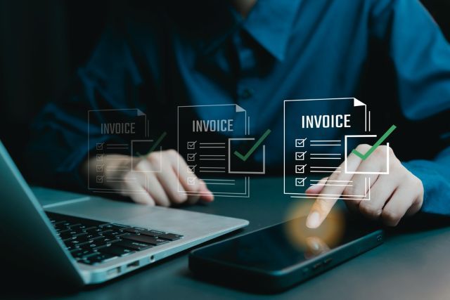 Man's hands tap on mobile phone next to laptop with electronic invoices