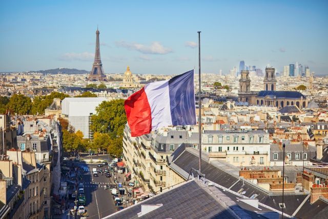 French flag flying above Parisian rooftops with Eiffel Tower in the distance top left.