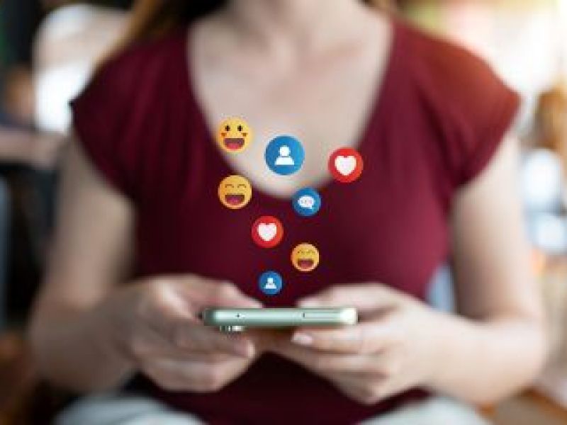 Girl using smart phone with social media emojis emerging from screen