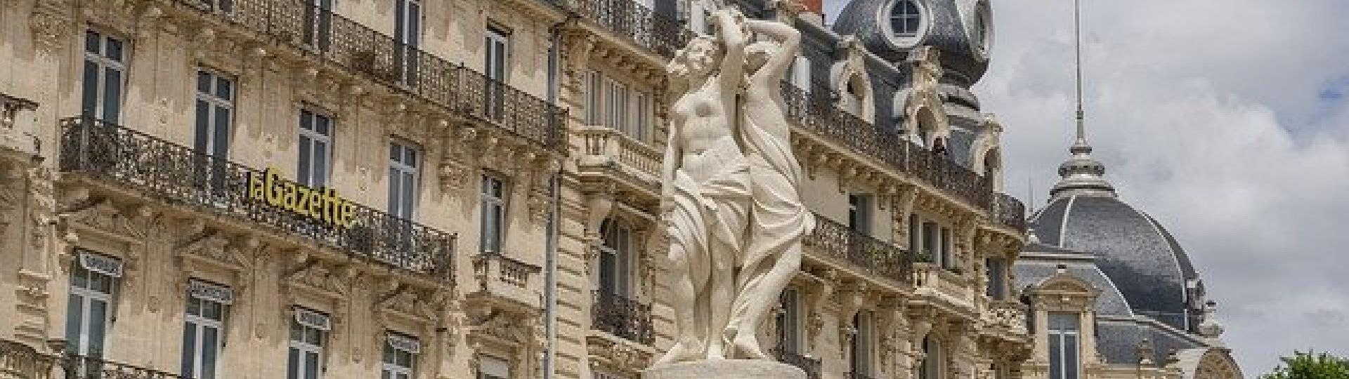 A classical statue of several women in a square in Montpellier, surrounded by traditional buildings